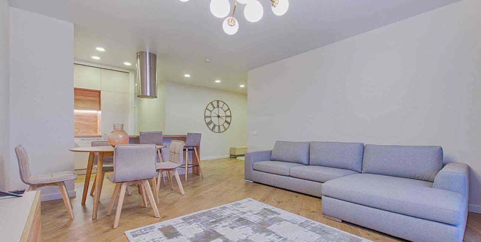 A modern living room with a gray sectional sofa, a dining area with a round table and chairs, and stylish lighting fixtures, creating a cozy and elegant ambiance.